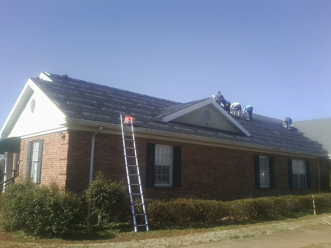 Crew tearing shingles off a brick ranch roof with a ladder set — Emergency Roof Repair work by our crew in Thayer