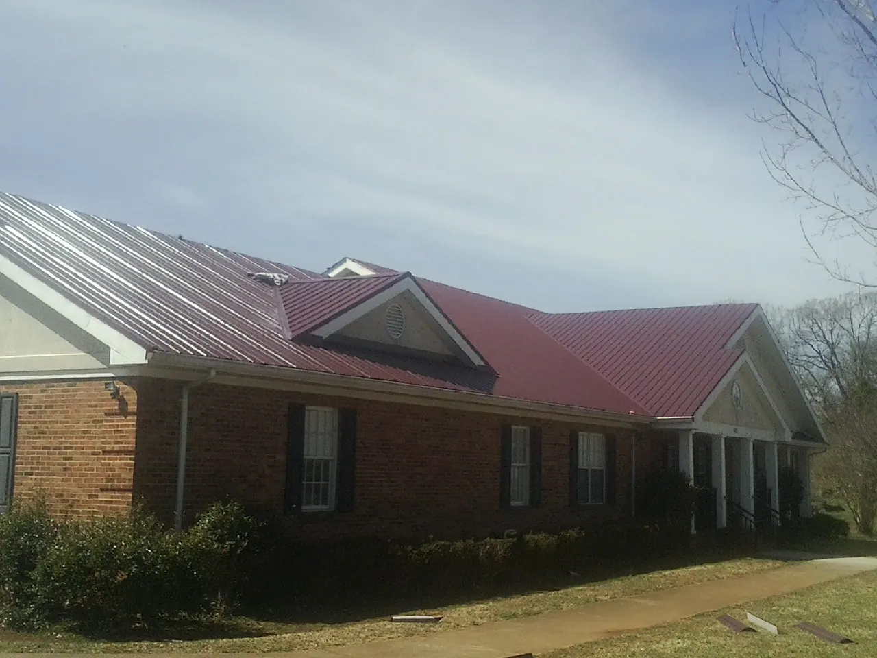 Red metal roof with gabled entries on a long brick building, from a Hail Damage Roof Repair job in Thayer