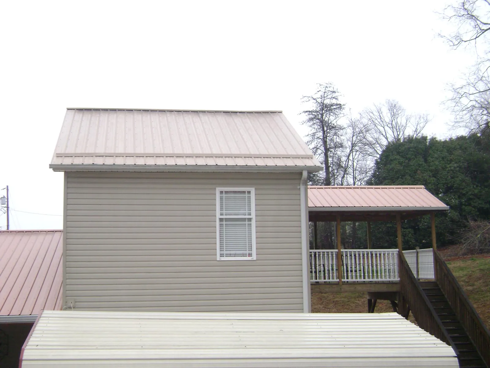 Tan metal roofs on a two story addition and attached porch, from a Roof Replacement job in Thayer