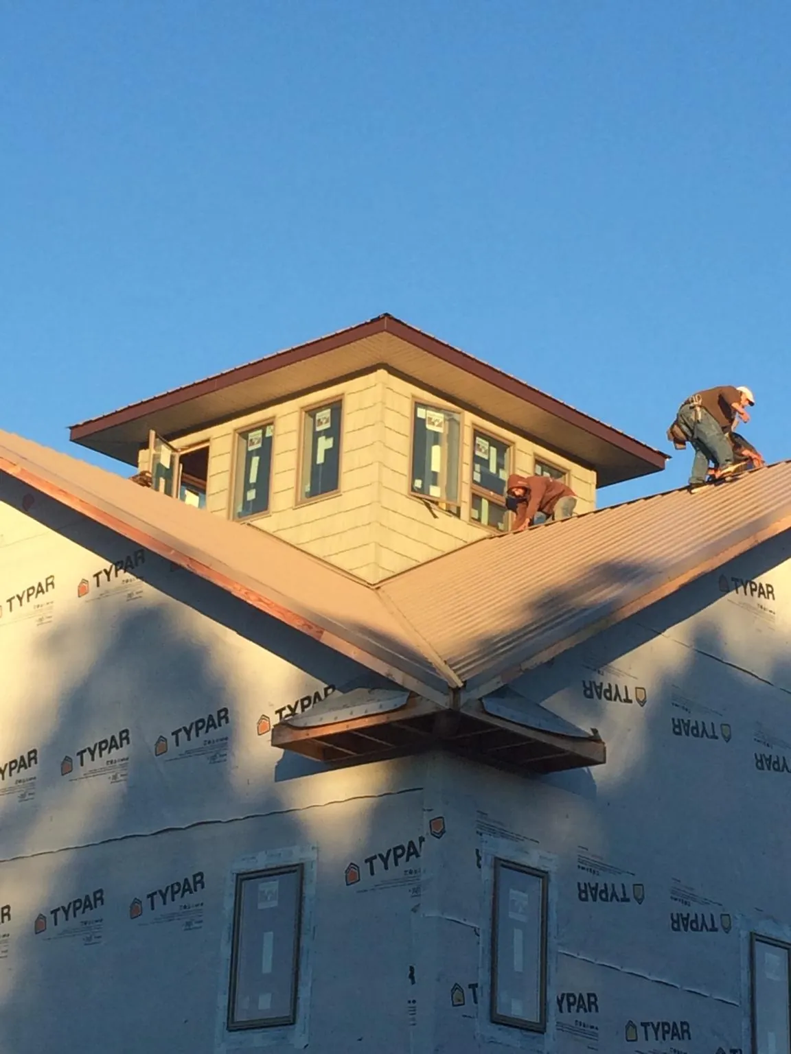 Roofers working around a rooftop cupola on a new metal roof at sunset — Roof Waterproofing in Thayer by Roofing Brothers